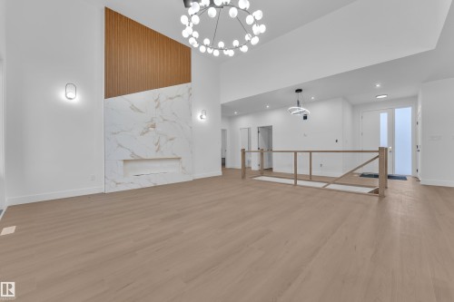 Unfurnished living room featuring a high ceiling, a chandelier, light wood-style flooring, and a high end fireplace - 215 Basin Court, Leduc, AB - Indoor Photo Showing Other Room