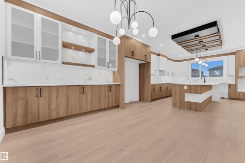 Two tone kitchen with a chandelier, a kitchen bar, two tone cabinets, light wood-type flooring, and an island with sink - 215 Basin Court, Leduc, AB - Indoor