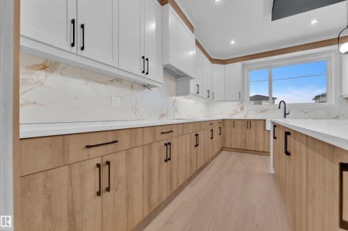 Kitchen with two tone color scheme, light wood-type flooring, light stone counters, recessed lighting, and backsplash - 215 Basin Court, Leduc, AB - Indoor Photo Showing Kitchen