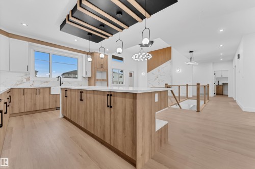 Two tone kitchen featuring a large island, light wood-type flooring, pendant lighting, light stone countertops, and two tone cabinets - 215 Basin Court, Leduc, AB - Indoor Photo Showing Kitchen With Upgraded Kitchen
