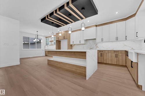 Two tone kitchen with dual tone cabinets, hanging lights, light stone countertops, a center island, and light wood finished floors - 215 Basin Court, Leduc, AB - Indoor Photo Showing Kitchen