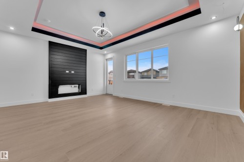 Spare room featuring light wood finished floors, a raised ceiling, a fireplace, and suspended lighting - 215 Basin Court, Leduc, AB - Indoor Photo Showing Other Room