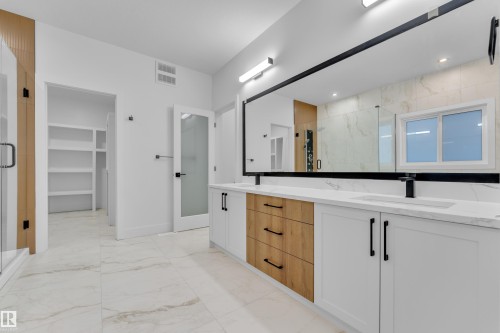 Full bathroom featuring a marble finish shower, light marble finish floors, double vanity, and a walk in closet - 215 Basin Court, Leduc, AB - Indoor Photo Showing Bathroom
