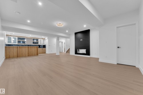Unfurnished living room featuring light wood-style flooring, recessed lighting, bar with sink, and a fireplace - 215 Basin Court, Leduc, AB - Indoor Photo Showing Other Room