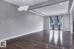 Empty room with a tray ceiling, dark wood-style floors, and hanging lights - 