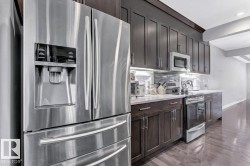 Kitchen with stainless steel appliances, dark wood finish cabinets, dark wood-style floors, decorative backsplash, and light stone countertops - 