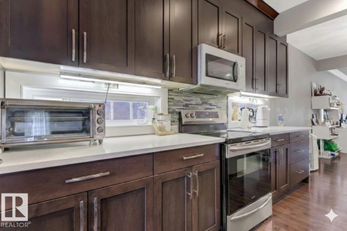 Kitchen with stainless steel electric range, white microwave, dark wood finish cabinetry, backsplash, and dark wood-style flooring - 10806 72 Avenue, Edmonton, AB - Indoor Photo Showing Kitchen