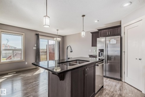 Kitchen featuring dark wood finish cabinets, stainless steel appliances, an island with sink, light wood-type flooring, and hanging light fixtures - 1669 Hammond Crescent, Edmonton, AB - Indoor Photo Showing Kitchen With Stainless Steel Kitchen With Double Sink With Upgraded Kitchen