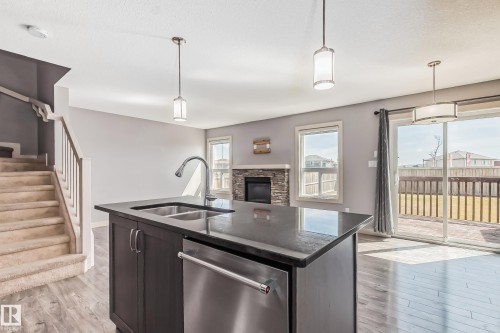Kitchen featuring a kitchen island with sink, dishwasher, a stone fireplace, pendant lighting, and a textured ceiling - 1669 Hammond Crescent, Edmonton, AB - Indoor Photo Showing Kitchen With Double Sink