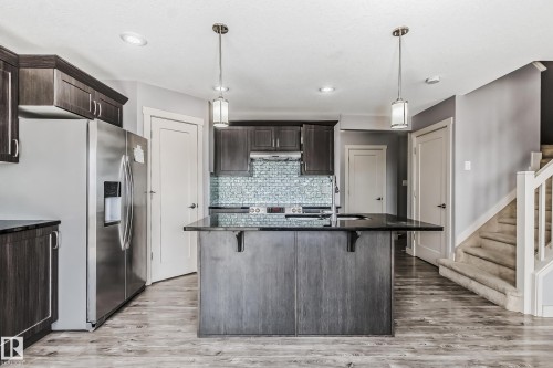 Kitchen with dark wood finish cabinetry, stainless steel fridge with ice dispenser, light wood-type flooring, dark stone counters, and a breakfast bar - 1669 Hammond Crescent, Edmonton, AB - Indoor Photo Showing Kitchen With Stainless Steel Kitchen With Upgraded Kitchen