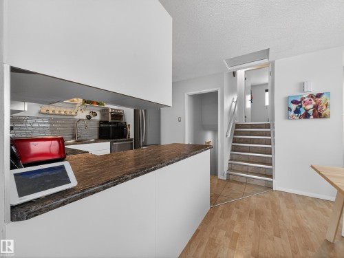 Kitchen featuring light wood-type flooring, white cabinets, dark countertops, stainless steel appliances, and a peninsula - 4603 32 Avenue, Edmonton, AB - Indoor