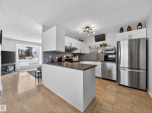 Kitchen with stainless steel appliances, white cabinetry, a peninsula, a textured ceiling, and backsplash - 4603 32 Avenue, Edmonton, AB - Indoor Photo Showing Kitchen With Upgraded Kitchen