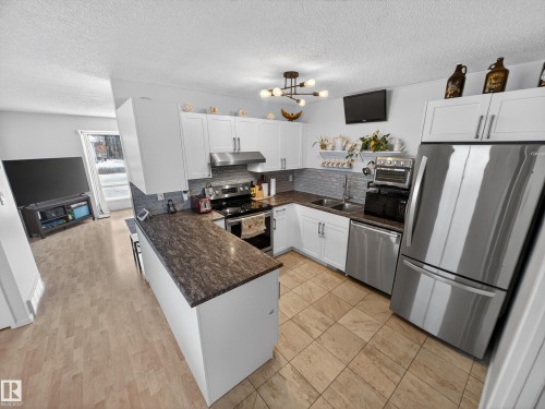 Kitchen featuring stainless steel appliances, white cabinets, a textured ceiling, and a peninsula - 4603 32 Avenue, Edmonton, AB - Indoor Photo Showing Kitchen With Double Sink