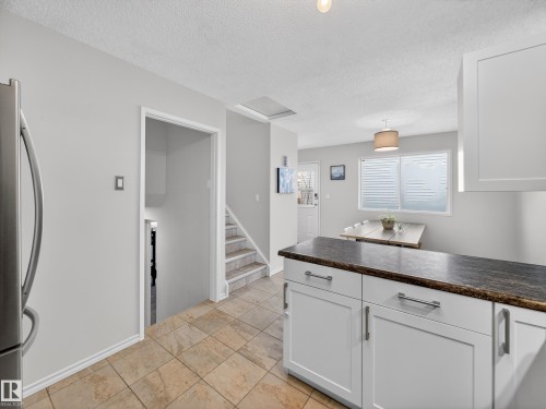 Kitchen with white cabinetry, freestanding refrigerator, dark countertops, and a textured ceiling - 4603 32 Avenue, Edmonton, AB - Indoor Photo Showing Kitchen