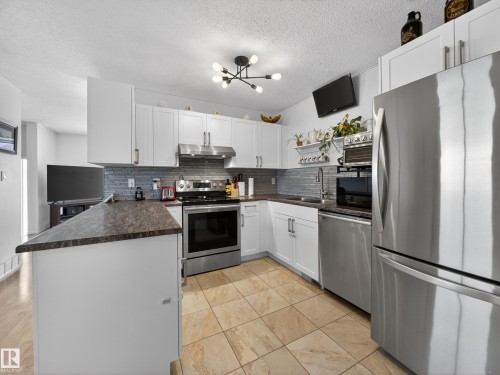 Kitchen featuring stainless steel appliances, dark countertops, a peninsula, white cabinets, and tasteful backsplash - 4603 32 Avenue, Edmonton, AB - Indoor Photo Showing Kitchen