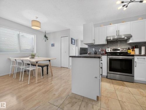 Kitchen featuring stainless steel range with electric stovetop, white cabinetry, a textured ceiling, tasteful backsplash, and hanging light fixtures - 4603 32 Avenue, Edmonton, AB - Indoor