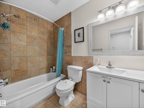 Full bath with a textured ceiling, vanity, shower / bath combo with shower curtain, and tile walls - 4603 32 Avenue, Edmonton, AB - Indoor Photo Showing Bathroom