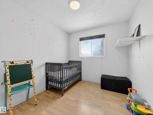 Bedroom with a crib, a textured ceiling, and light wood-style floors - 4603 32 Avenue, Edmonton, AB - Indoor Photo Showing Bedroom