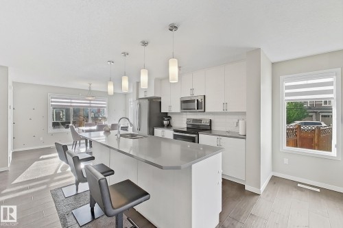 Kitchen featuring stainless steel appliances, white cabinets, light wood finished floors, and decorative light fixtures - 4303 Prowse Link, Edmonton, AB - Indoor Photo Showing Kitchen With Double Sink With Upgraded Kitchen