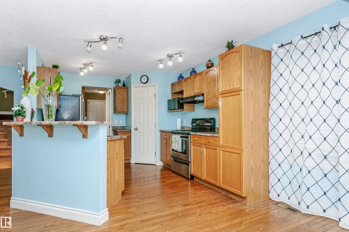 Kitchen with stainless steel appliances, a breakfast bar, light wood finished floors, and a textured ceiling - 607 Windross Crescent, Edmonton, AB - Indoor Photo Showing Kitchen