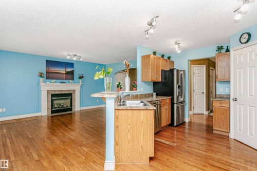 Kitchen featuring open floor plan, a peninsula, a fireplace, light wood finished floors, and a textured ceiling - 607 Windross Crescent, Edmonton, AB - Indoor Photo Showing Kitchen With Fireplace With Double Sink