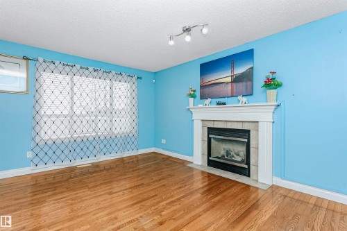 Unfurnished living room with wood finished floors, a textured ceiling, and a tiled fireplace - 607 Windross Crescent, Edmonton, AB - Indoor Photo Showing Living Room With Fireplace