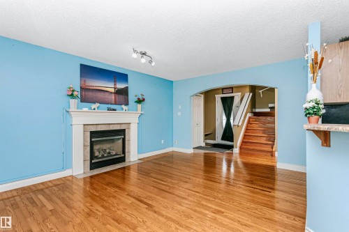 Unfurnished living room featuring arched walkways, light wood-style floors, a tiled fireplace, and a textured ceiling - 607 Windross Crescent, Edmonton, AB - Indoor Photo Showing Living Room With Fireplace