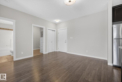 Unfurnished bedroom featuring freestanding refrigerator, ensuite bath, dark wood-style floors, and a closet - 206 812 Welsh Drive, Edmonton, AB - Indoor
