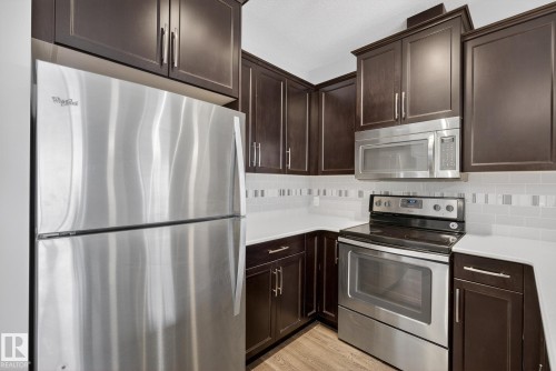 Kitchen with stainless steel appliances, dark wood finish cabinets, light countertops, and decorative backsplash - 206 812 Welsh Drive, Edmonton, AB - Indoor Photo Showing Kitchen With Stainless Steel Kitchen