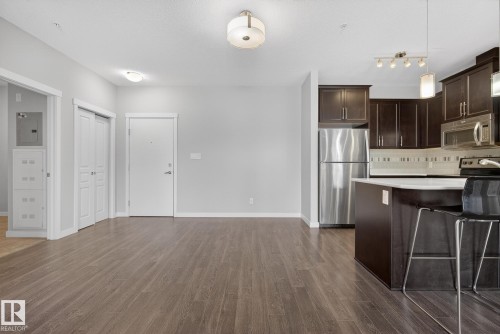 Kitchen featuring dark wood finish cabinets, light countertops, stainless steel appliances, backsplash, and dark wood-style flooring - 206 812 Welsh Drive, Edmonton, AB - Indoor Photo Showing Kitchen