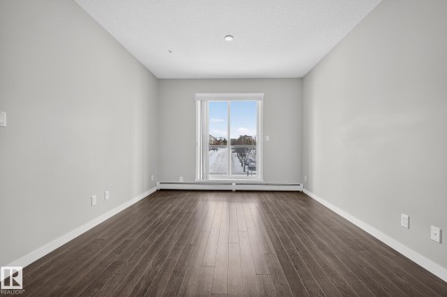 Empty room with dark wood-style flooring, a baseboard radiator, and a textured ceiling - 206 812 Welsh Drive, Edmonton, AB - Indoor Photo Showing Other Room
