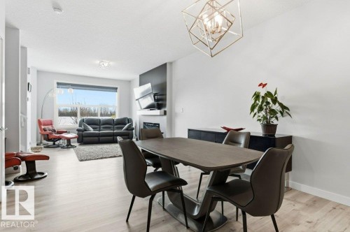 Dining area with light wood finished floors, a chandelier, a glass covered fireplace, and a textured ceiling - 8018 Kiriak Link, Edmonton, AB - Indoor Photo Showing Dining Room