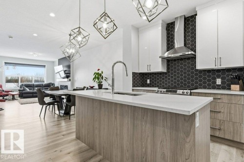 Kitchen featuring decorative light fixtures, a center island with sink, light wood-style flooring, light stone countertops, and two tone cabinetry - 8018 Kiriak Link, Edmonton, AB - Indoor Photo Showing Kitchen With Upgraded Kitchen