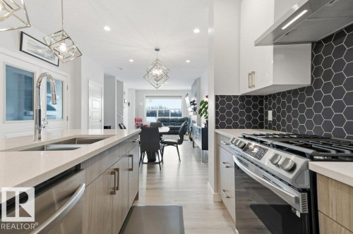 Kitchen featuring stainless steel appliances, exhaust hood, light stone countertops, modern cabinets, and light wood-style flooring - 8018 Kiriak Link, Edmonton, AB - Indoor Photo Showing Kitchen With Upgraded Kitchen