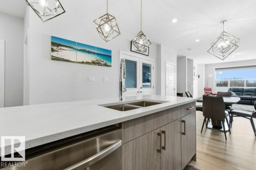 Kitchen featuring stainless steel dishwasher, light stone countertops, suspended lighting, light wood-style floors, and french doors - 8018 Kiriak Link, Edmonton, AB - Indoor