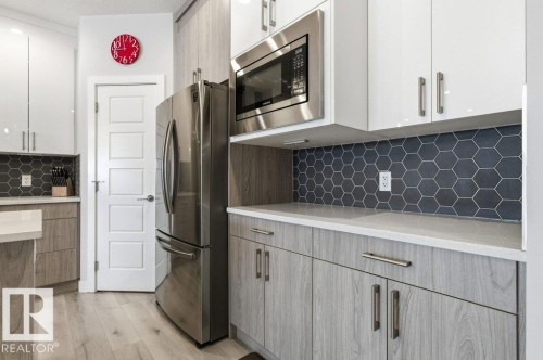 Two tone kitchen featuring stainless steel appliances, decorative backsplash, two tone cabinets, light stone counters, and modern cabinets - 8018 Kiriak Link, Edmonton, AB - Indoor Photo Showing Kitchen