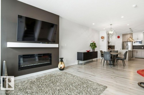 Living Room featuring a glass covered fireplace, light wood-style floors, and suspended lighting - 8018 Kiriak Link, Edmonton, AB - Indoor Photo Showing Living Room With Fireplace