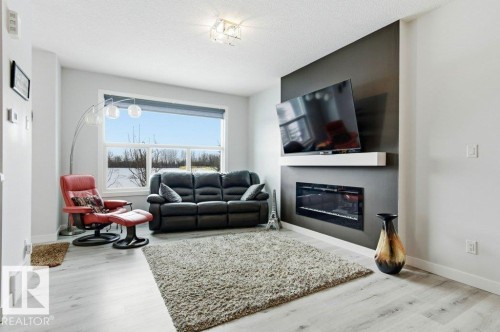 Living area featuring light wood-style floors, a glass covered fireplace, and a textured ceiling - 8018 Kiriak Link, Edmonton, AB - Indoor Photo Showing Living Room With Fireplace
