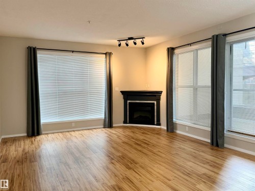 Unfurnished living room with light wood-style flooring, a fireplace, and rail lighting - 115 11039 83 Avenue, Edmonton, AB - Indoor Photo Showing Living Room With Fireplace