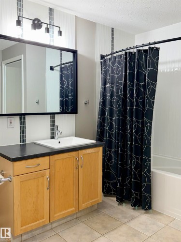 Full bathroom with vanity, a textured ceiling, light tile patterned floors, and shower / tub combo with curtain - 115 11039 83 Avenue, Edmonton, AB - Indoor