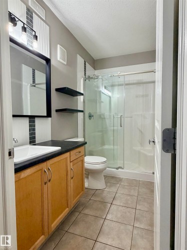 Full bathroom featuring vanity, a shower stall, light tile patterned flooring, and a textured ceiling - 115 11039 83 Avenue, Edmonton, AB - Indoor Photo Showing Bathroom