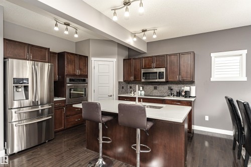 Kitchen featuring stainless steel appliances, a kitchen island with sink, dark wood finish cabinetry, dark wood-type flooring, and tasteful backsplash - 115 57 Street, Edmonton, AB - Indoor Photo Showing Kitchen