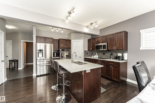 Kitchen with stainless steel appliances, a breakfast bar, decorative backsplash, dark wood finished floors, and a textured ceiling - 115 57 Street, Edmonton, AB - Indoor Photo Showing Kitchen With Double Sink