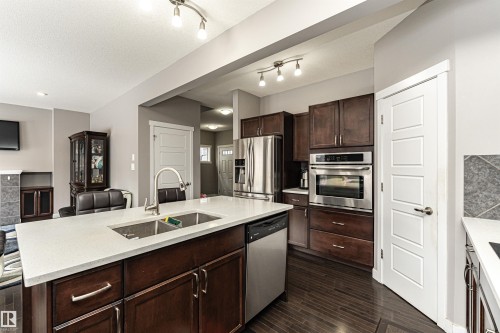 Kitchen with stainless steel appliances, open floor plan, dark wood finish cabinets, dark wood finished floors, and light stone counters - 115 57 Street, Edmonton, AB - Indoor Photo Showing Kitchen With Double Sink With Upgraded Kitchen