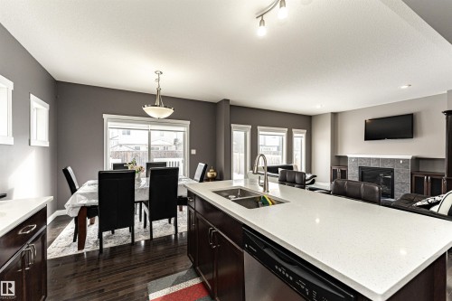 Kitchen featuring a tile fireplace, open floor plan, stainless steel dishwasher, a center island with sink, and light stone counters - 115 57 Street, Edmonton, AB - Indoor Photo Showing Kitchen With Double Sink