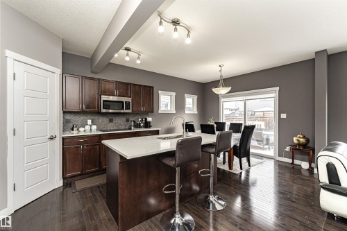 Kitchen featuring dark wood finish cabinets, a center island with sink, a breakfast bar area, stainless steel microwave, and decorative light fixtures - 115 57 Street, Edmonton, AB - Indoor