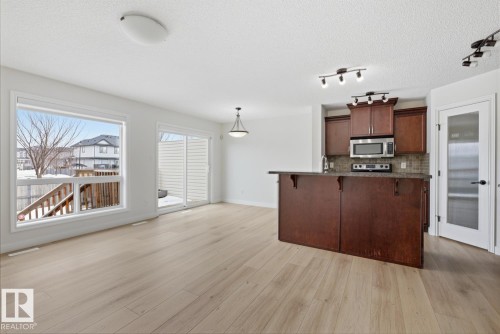 Kitchen with a kitchen breakfast bar, stainless steel appliances, a kitchen island with sink, a textured ceiling, and light wood-style flooring - 73 Keystone Crescent Crescent, Leduc, AB - Indoor Photo Showing Kitchen