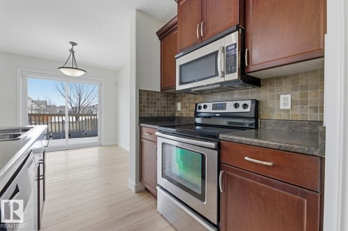 Kitchen featuring stainless steel appliances, hanging light fixtures, dark countertops, light wood finished floors, and a textured ceiling - 73 Keystone Crescent Crescent, Leduc, AB - Indoor Photo Showing Kitchen With Double Sink
