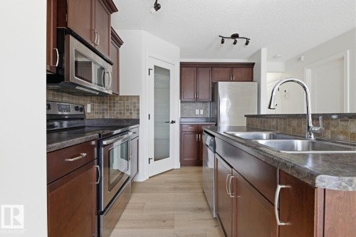 Kitchen featuring stainless steel appliances, dark countertops, decorative backsplash, light wood-style floors, and track lighting - 73 Keystone Crescent Crescent, Leduc, AB - Indoor Photo Showing Kitchen With Double Sink