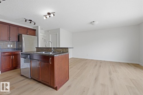 Kitchen featuring a center island with sink, stainless steel appliances, tasteful backsplash, light wood-style flooring, and a textured ceiling - 73 Keystone Crescent Crescent, Leduc, AB - Indoor Photo Showing Kitchen With Double Sink